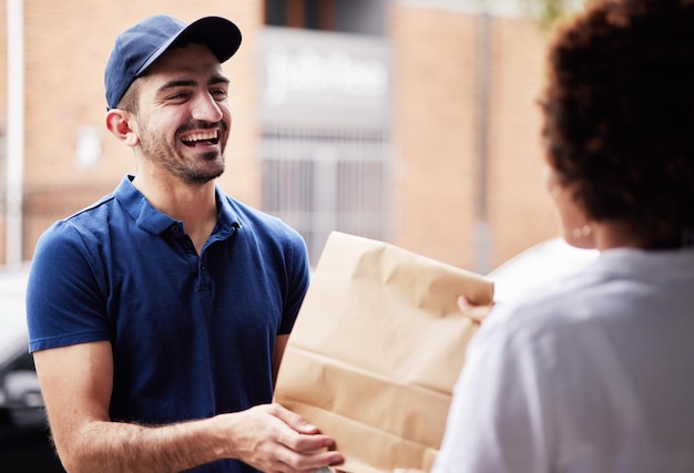 Foto pacchetto uomo di consegna felice e un cliente alla porta con un sacchetto di carta per il commercio elettronico e la spedizione logistica acquisti online e merci o corriere ridendo e dando a una donna un ordine di fast food