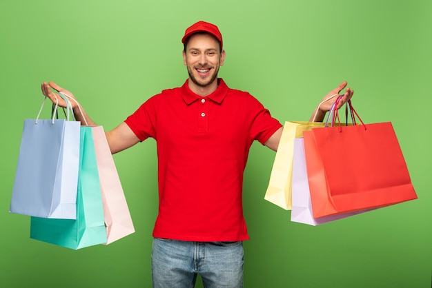 Happy delivery man in red uniform holding shopping bags on green