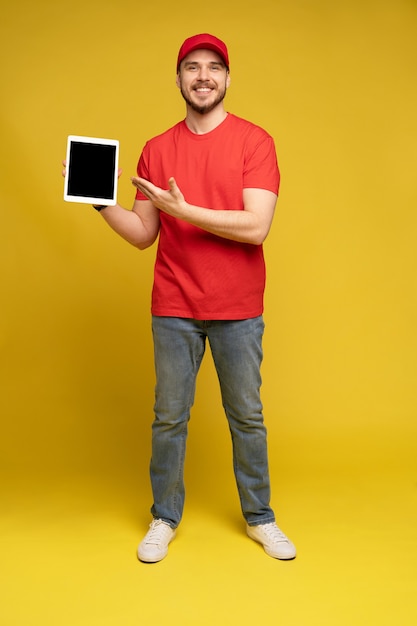 Happy delivery man with tablet in studio isolated yellow wall