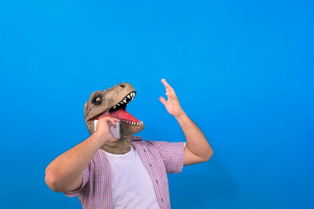 Happy dinosaur head man talking on cellphone on isolated blue background