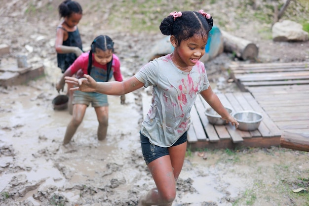 Happy dirty African and Asian girls run chase in puddle mud together at outdoor summer camp learning