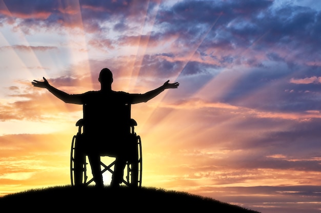 Happy disabled man in a wheelchair on a hill enjoying the sunset. the concept of happy disabled