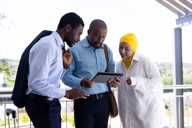 Happy diverse business people using tablet and talking outside office. Global business, finances and office concept.