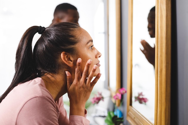 バスルームで幸せな多様なカップル、前景で顔をきれいにする鏡を見ている女性