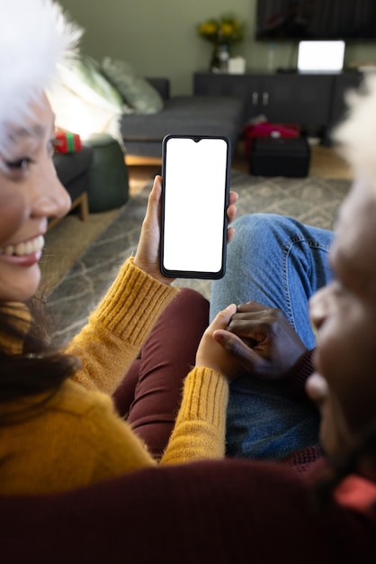 Happy diverse couple in christmas hats having smartphone video call copy space screen