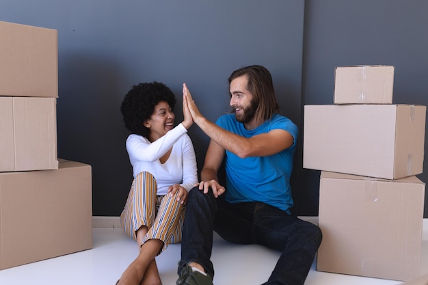 Happy diverse couple moving house sitting and high fiving