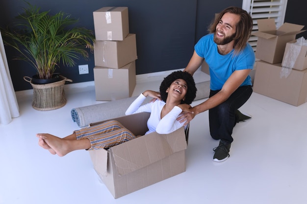 Happy diverse couple moving house smiling and playing with cartons