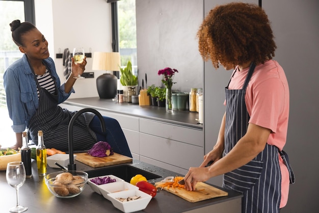 Happy diverse couple preparing meal, chopping vegetables, drinking wine and talking in kitchen