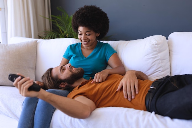 Happy diverse couple sitting on sofa embracing and watching tv