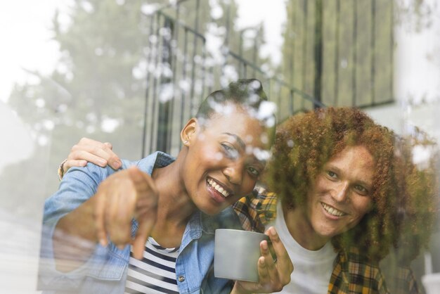 Photo happy diverse couple sitting on stairs at home, drinking coffee, embracing and looking out of window. togetherness, relationship, free time, lifestyle and domestic life, unaltered.