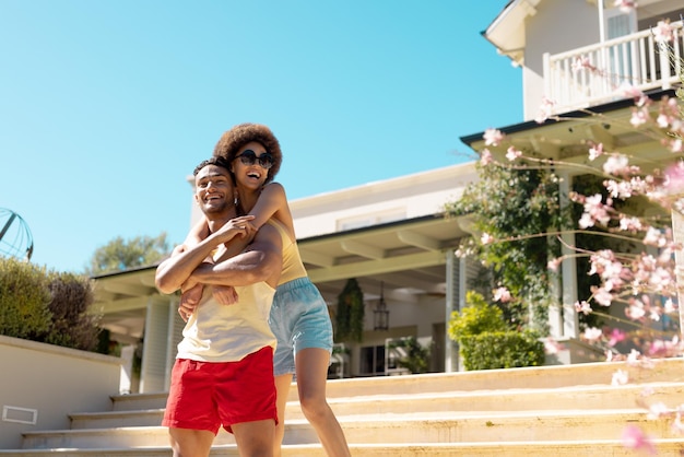 Happy diverse couple standing outside the house, embracing and smiling. Lifestyle, friendship, party time, vacation and summer.