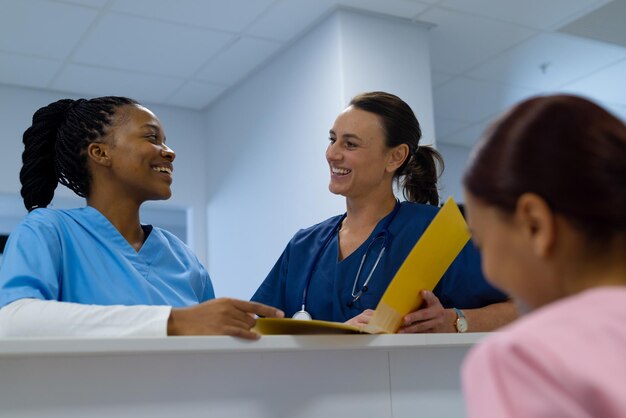 Happy diverse female doctors wearing scrubs talking at reception desk at hospital