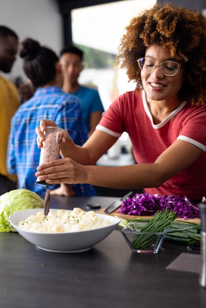 Photo happy diverse group of friends seasoning and cooking in kitchen