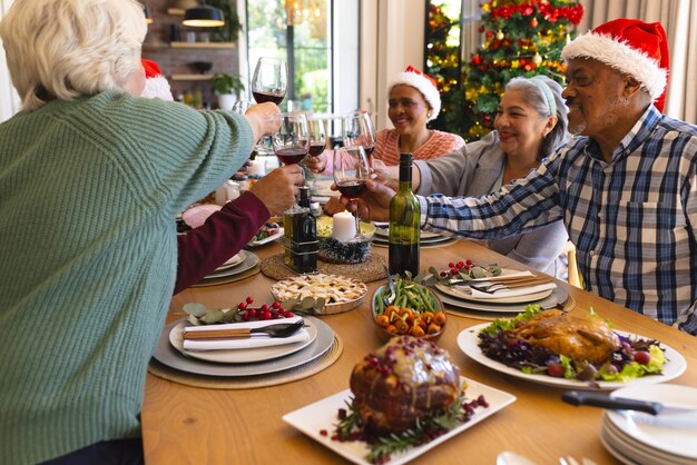 Photo happy diverse group of senior friends toasting at christmas dinner in sunny dining room at home