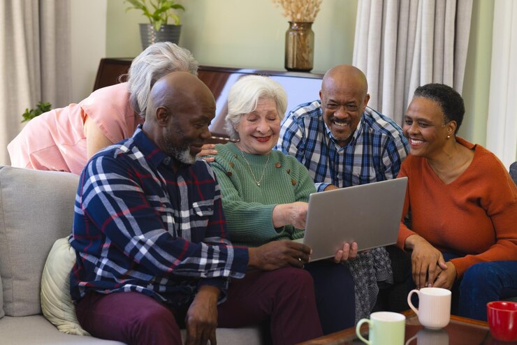 Happy diverse group of senior friends using laptop discussing in sunny living room