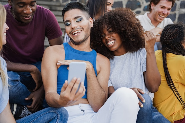 happy diverse people having fun using mobile phone outdoor in the city - focus on transgender man face