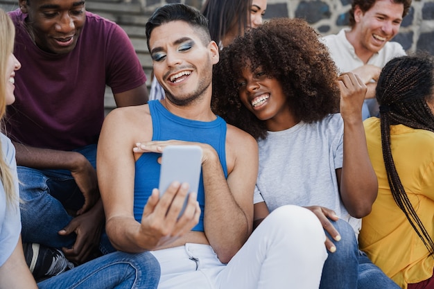 Felici persone diverse che si divertono usando il telefono cellulare all'aperto in città - concentrati sul volto dell'uomo transgender