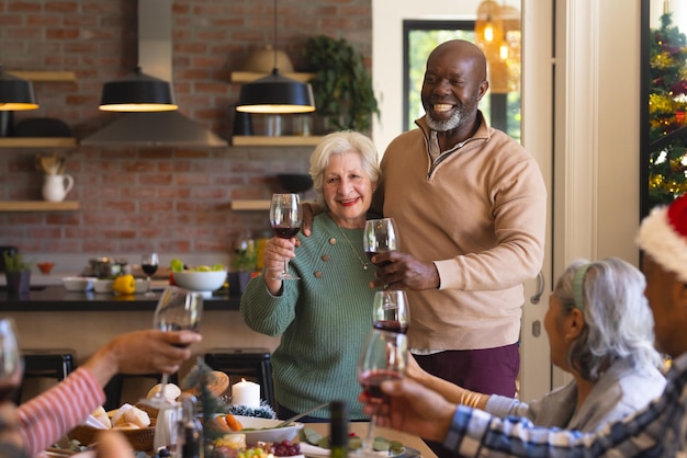 happy diverse senior couple of friends toasting at christmas dinner in sunny dining room