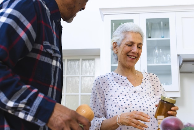 Photo happy diverse senior couple unpacking groceries in kitchen