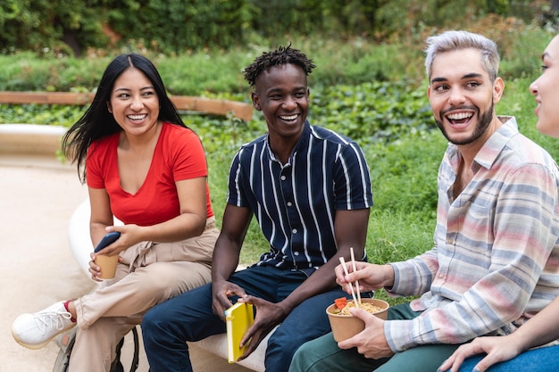 Happy diverse students having fun eating takeaway food outdoor\
at university park