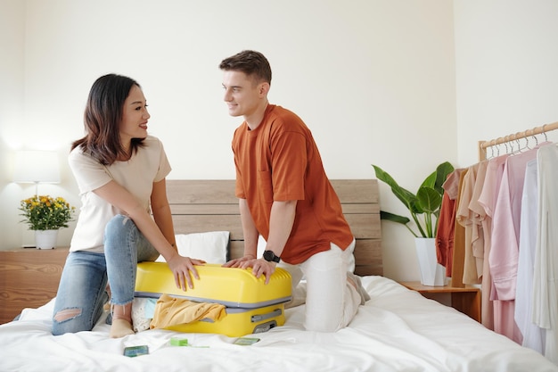 Happy diverse young couple trying to close full suitcase packed for vacation