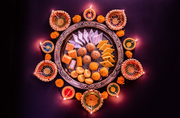 Happy diwali - flower rangoli con dolci o mithai e diya in ciotole per diwali o qualsiasi altro festival in india, messa a fuoco selettiva