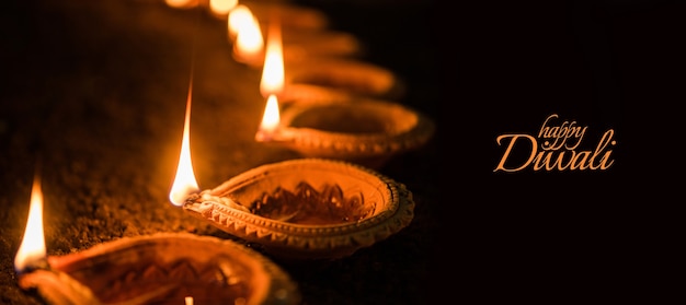 Photo happy diwali greeting card design using beautiful lit diya or clay oil lamps