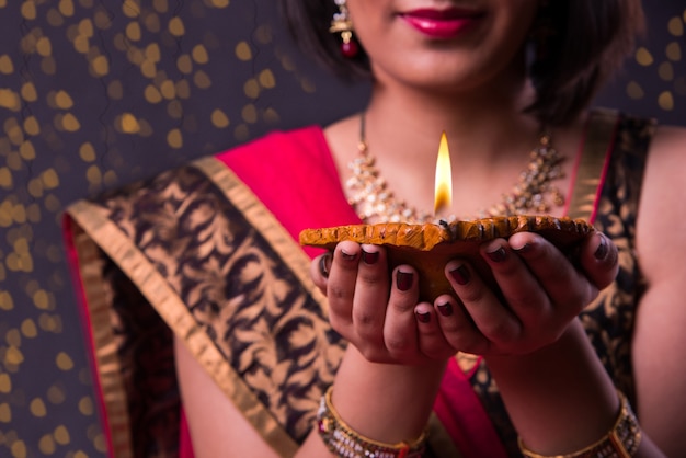 Happy diwali greeting card showing indian beautiful Girl holding a diya or Terracotta Oil Lamp over black background