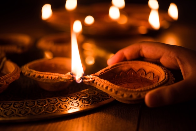 Happy diwali - Hand holding or lighting or arranging diwali diya or clay lamp in brass plate, selective focus