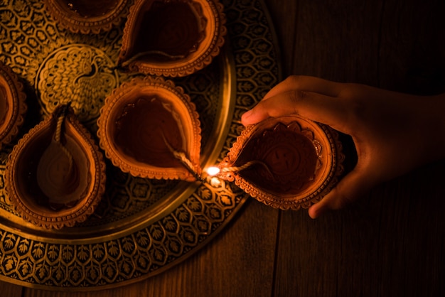 Happy diwali - Hand holding or lighting or arranging diwali diya or clay lamp in brass plate, selective focus