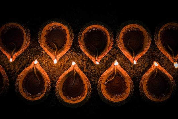 Foto happy diwali - molte lampade diya o olio in terracotta disposte su una superficie di argilla o macinate in una linea o forma curva o a zigzag, messa a fuoco selettiva