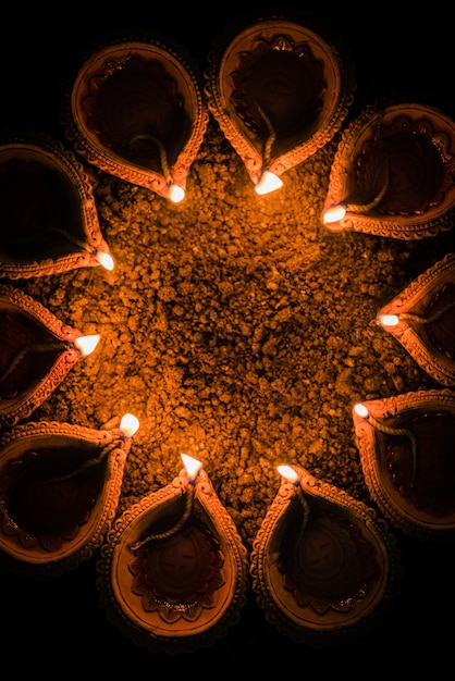 Happy Diwali - many Terracotta diya or oil lamps arranged over clay surface or ground in one line or curved or zigzag form, selective focus