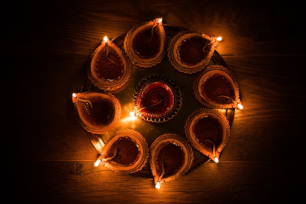 Happy Diwali - many Terracotta diya or oil lamps arranged over clay surface or ground in one line or curved or zigzag form, selective focus