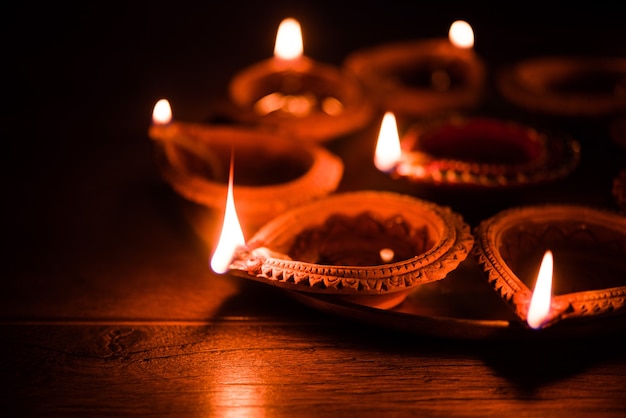 Happy Diwali - many Terracotta diya or oil lamps arranged over clay surface or ground in one line or curved or zigzag form, selective focus