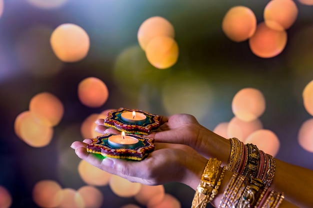 Happy Diwali - Woman hands with henna holding lit candle isolated on dark background. Clay Diya lamps lit during Dipavali, Hindu festival of lights celebration. Copy space for text.