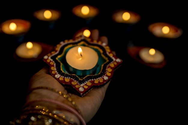 Happy Diwali Woman hands with henna holding lit candle isolated on dark background Clay Diya lamps lit during Dipavali Hindu festival of lights celebration Copy space for text