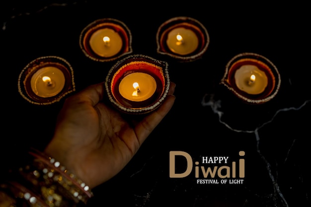 Foto happy diwali mani di donna con henné che tengono candela accesa isolata su sfondo scuro lampade clay diya accese durante la celebrazione del festival delle luci indù dipavali copia spazio per il testo