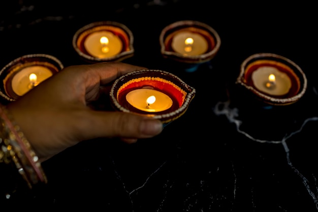 Foto happy diwali mani di donna con henné che tengono candela accesa isolata su sfondo scuro lampade clay diya accese durante la celebrazione del festival delle luci indù dipavali copia spazio per il testo