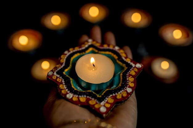 Foto happy diwali mani di donna con henné che tengono candela accesa isolata su sfondo scuro lampade clay diya accese durante la celebrazione del festival delle luci indù dipavali copia spazio per il testo