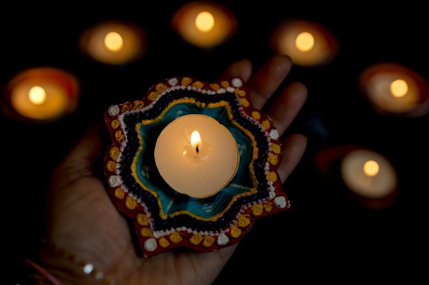 Foto happy diwali mani di donna con henné che tengono candela accesa isolata su sfondo scuro lampade clay diya accese durante la celebrazione del festival delle luci indù dipavali copia spazio per il testo