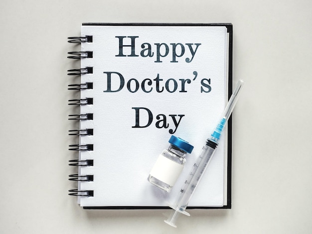 Happy doctor's day siringhe fiale per iniezione e un blocco note sdraiato sul tavolo vista interna del primo piano dall'alto foto dello studio della luce diurna concetto di assistenza sanitaria