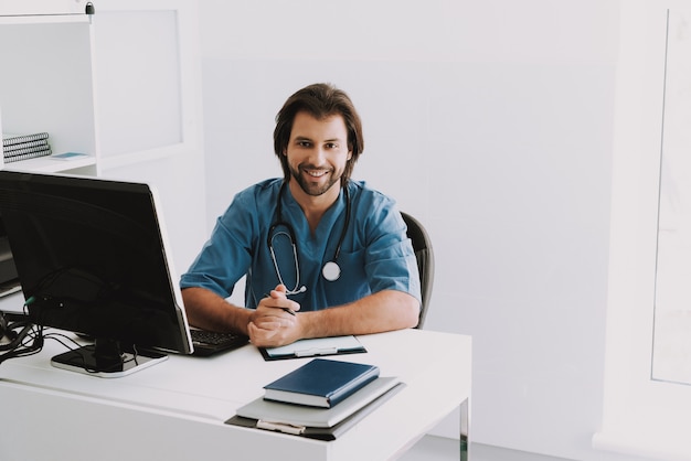 Happy Doctor Sitting at Desk Waiting for Patient.