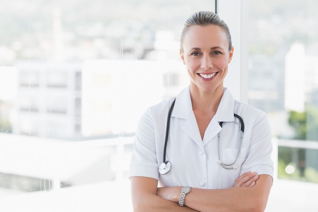 Happy doctor smiling at camera with arms crossed in medical office 