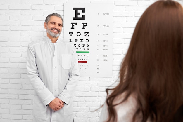 Photo happy doctor smiling, posing near eye chart in clinic.