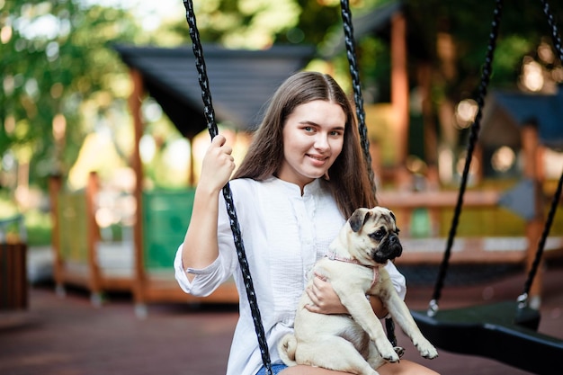 幸せな犬と女の子女の子は犬と遊んでいます夏の公園でパグ犬と一緒に歩いている若い女性パグの肖像美しいパグの子犬の肖像犬は地面に横たわっています