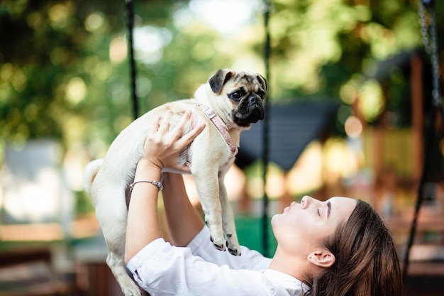 Felice cane e ragazza la ragazza sta giocando con un cane giovane donna che cammina con un carlino nel parco estivo ritratto di un carlino ritratto di un bellissimo cucciolo di carlino il cane è sdraiato a terra