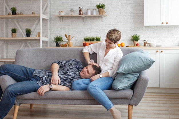 Счастливая мечтательная молодая кавказская пара отдыхает на диване в дизайнерской гостиной, расслабляясь и обнимаясь