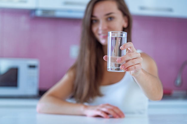 自宅のキッチンで手にきれいな精製水ガラスを保持している幸せな飲む女性