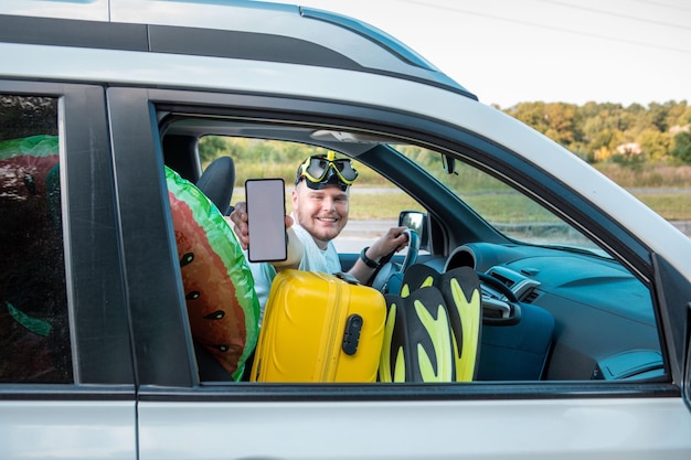 Happy driver man car full of vacation stuff holding phone with white screen