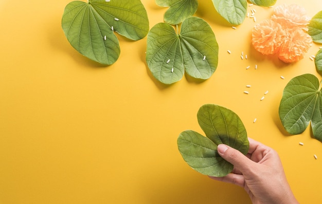 Happy Dussehra Hand holding green leaf yellow flowers and rice on yellow paper background Dussehra Indian Festival concept